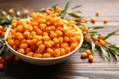 Photo of Fresh ripe sea buckthorn in bowl on wooden table, closeup