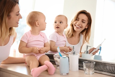 Photo of Young woman with toothbrush and daughter near mirror in bathroom