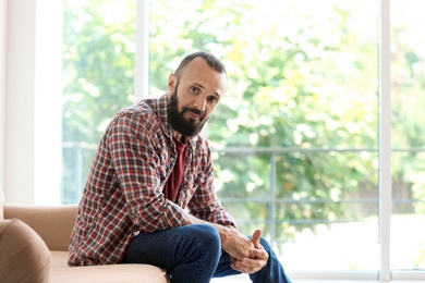 Photo of Portrait of handsome mature man sitting on sofa at home