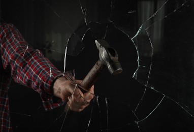 Photo of Man breaking window with hammer on black background, closeup