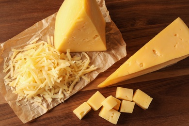 Photo of Grated and cut delicious cheese on wooden background, top view