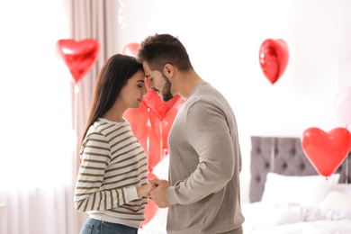 Photo of Lovely young couple in bedroom decorated with heart shaped balloons. Valentine's day celebration