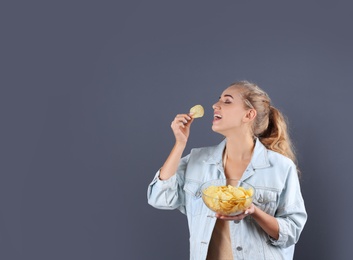 Photo of Woman eating potato chips on grey background. Space for text