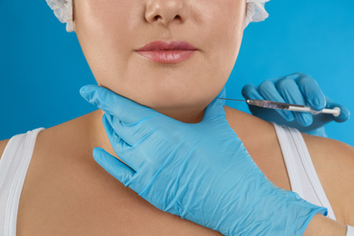 Photo of Woman with double chin getting injection on blue background, closeup. Cosmetic surgery