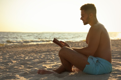 Photo of Young man reading book on sandy beach near sea