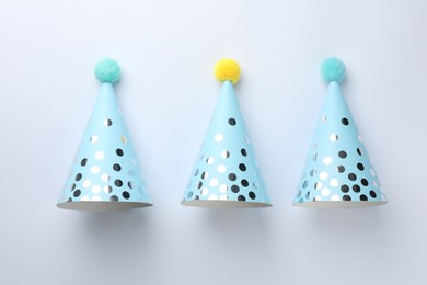 Photo of Colorful party hats with pompoms on light background, top view