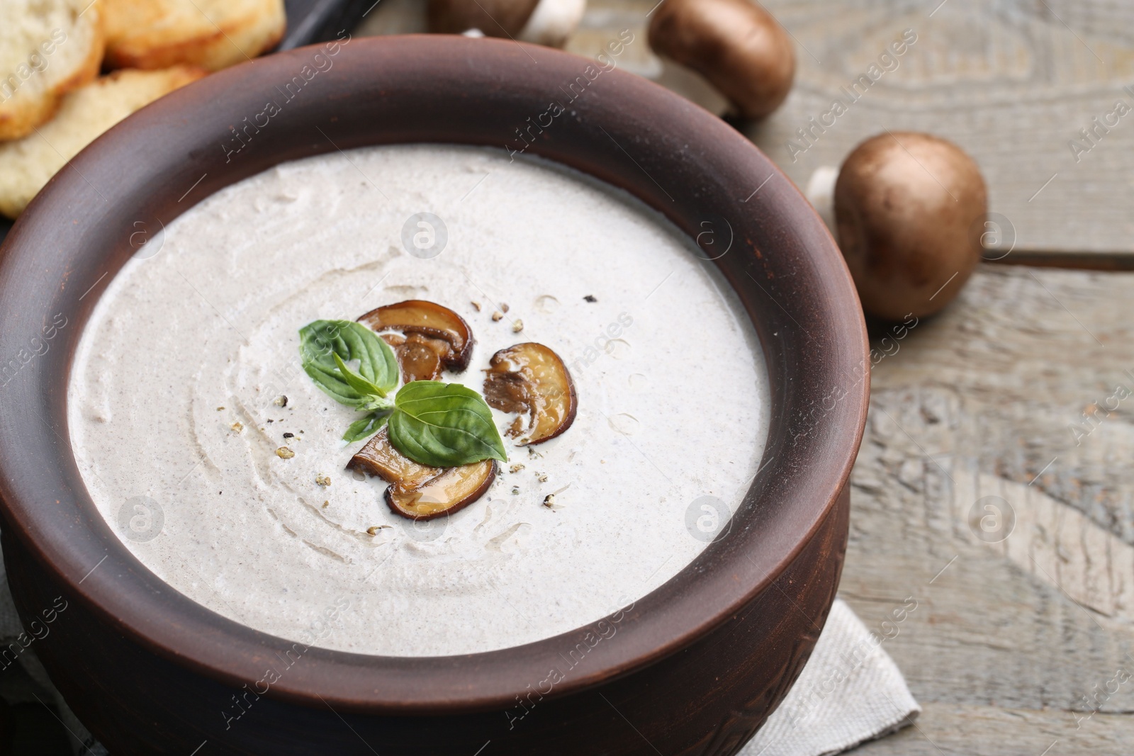 Photo of Fresh homemade mushroom soup in ceramic pot on wooden table, closeup