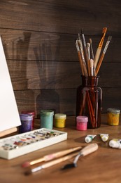 Photo of Easel with canvas and art supplies on wooden table