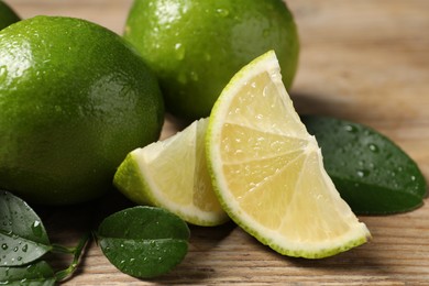 Photo of Fresh limes and green leaves with water drops on wooden table, closeup
