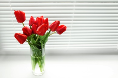 Photo of Bouquet of beautiful tulips in vase near window with blinds. Space for text