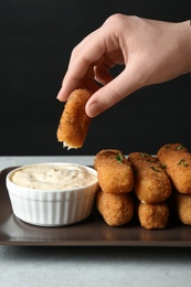 Photo of Woman dipping cheese stick into sauce at table, closeup
