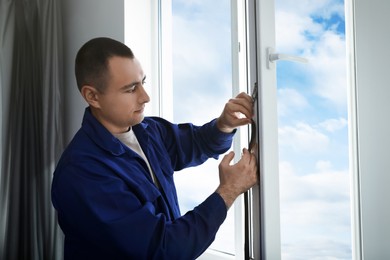 Photo of Construction worker putting sealing foam tape on window indoors