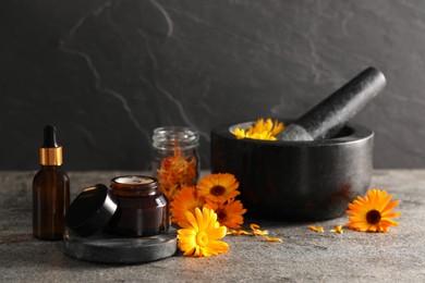 Photo of Jar of cream, bottle of essential oil, mortar and beautiful calendula flowers on grey table