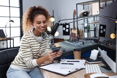 Photo of African American woman with smartphone working as radio host in modern studio