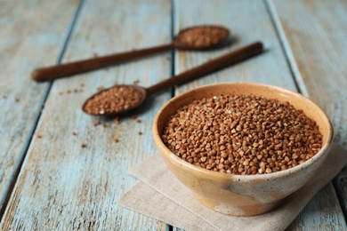Photo of Uncooked buckwheat in bowl on table. Space for text