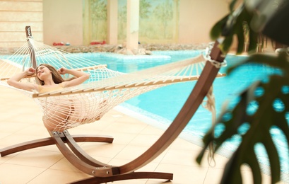 Photo of Young woman resting in hammock near pool