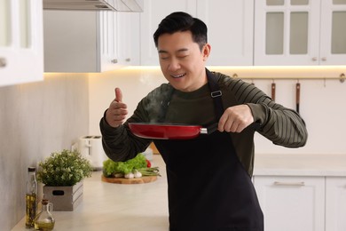 Photo of Man with frying pan smelling dish after cooking in kitchen