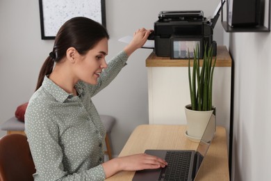 Photo of Woman using modern printer at workplace indoors