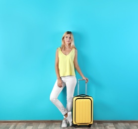 Photo of Woman with suitcase near color wall. Vacation travel