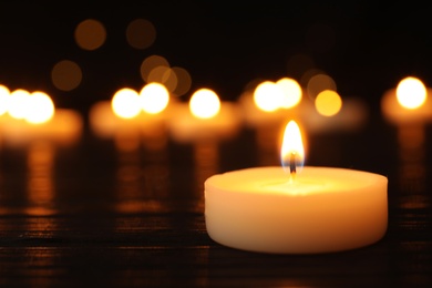 Photo of Burning candle on black table against blurred background, space for text