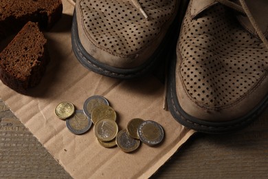 Photo of Poverty. Old shoes, coins, pieces of bread and cardboard sheet on wooden table, above view