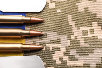 Photo of Military ID tags, bullets and Ukrainian flag on pixel camouflage, flat lay. Space for text