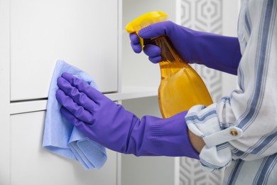 Woman cleaning white surface with detergent and rag indoors, closeup