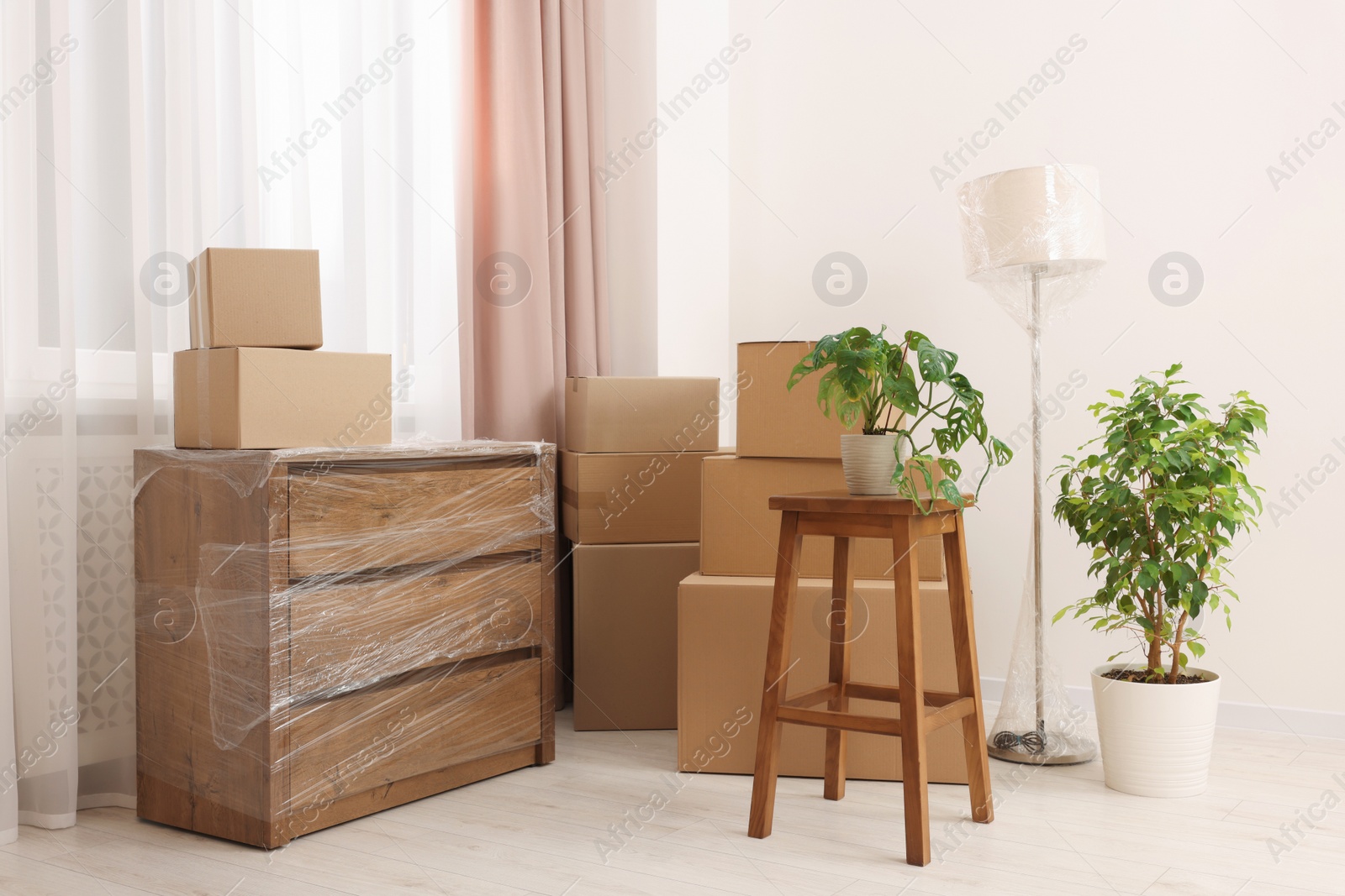 Photo of Boxes, lamp and chest of drawers wrapped in stretch film indoors