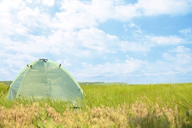 Photo of Modern camping tent in green field on sunny day. Space for text