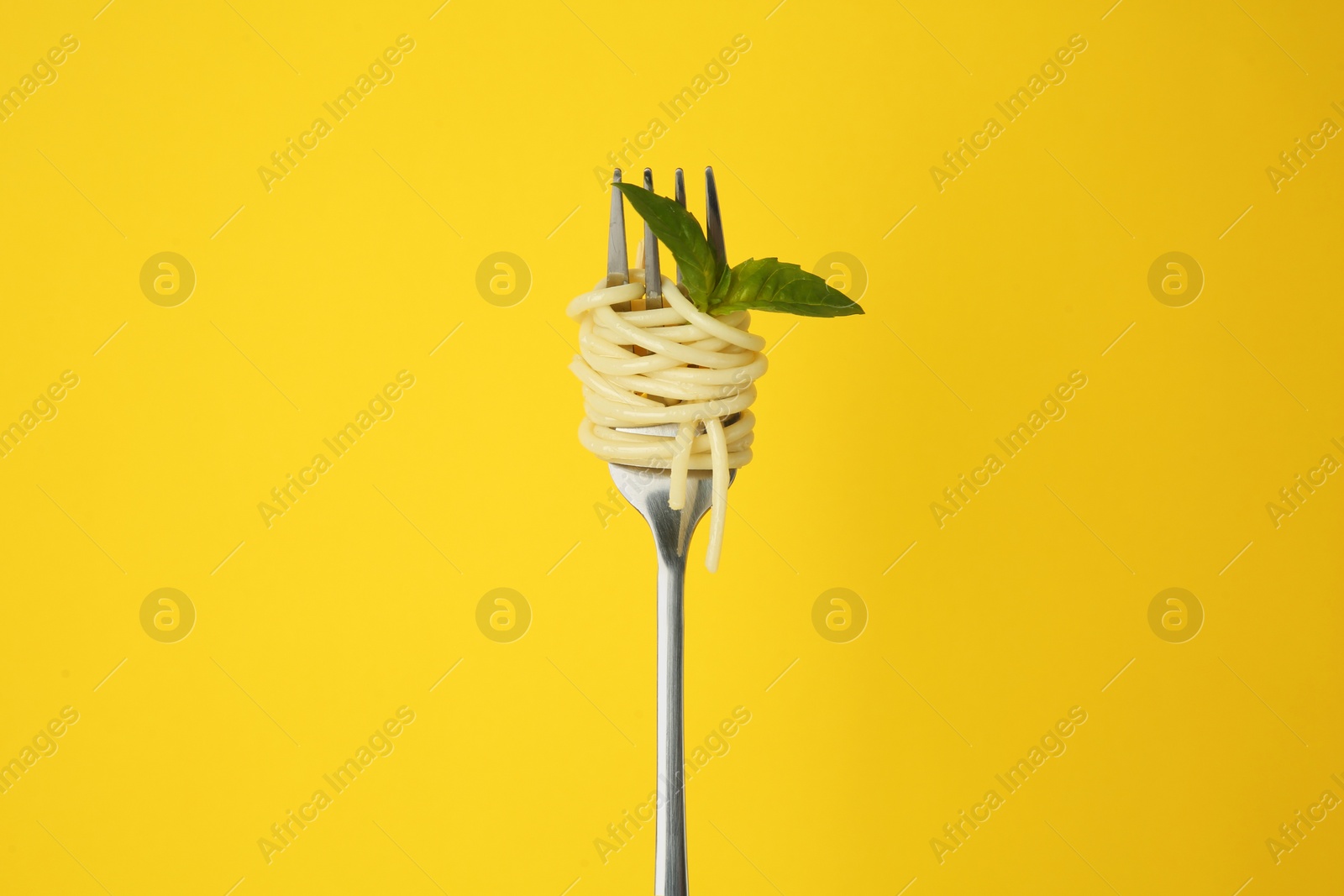 Photo of Fork with tasty pasta and basil leaves on yellow background