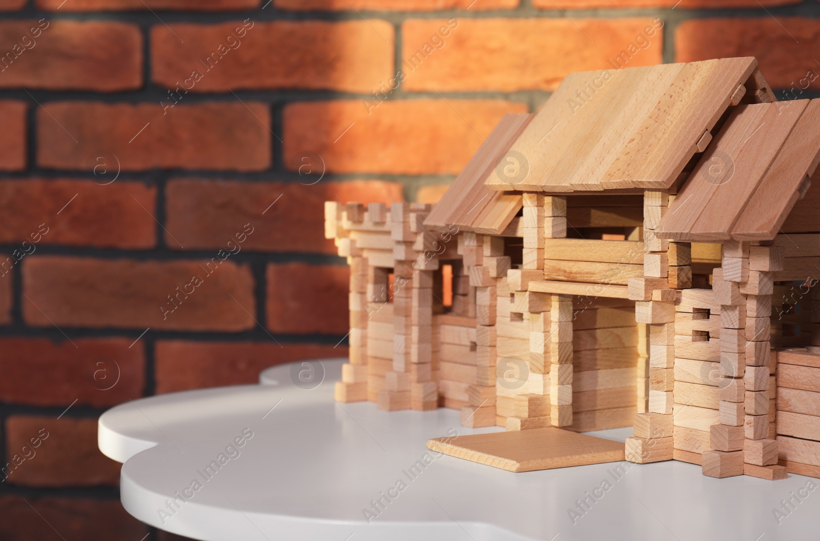 Photo of Wooden castle on white table near brick wall, space for text. Children's toy