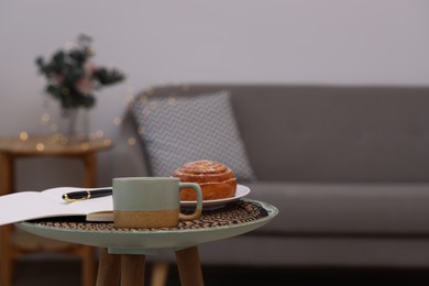 Cup of drink, pastry and notebook on coffee table indoors. Space for text