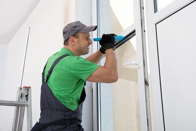 Photo of Worker in uniform installing double glazing window indoors