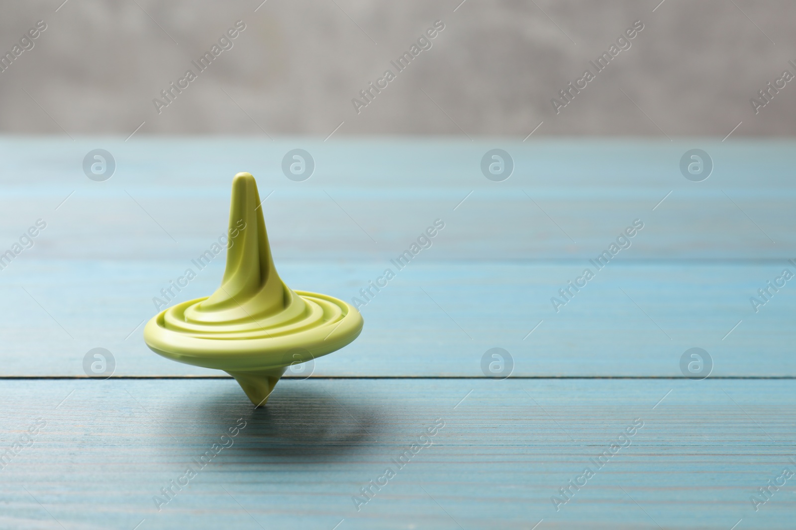 Photo of Bright spinning top on light blue wooden table, closeup. Space for text