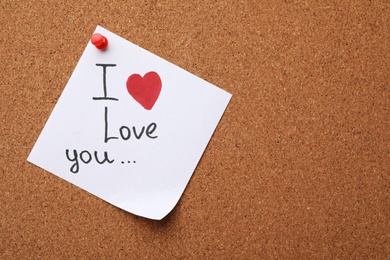 Photo of Paper sheet with words I LOVE YOU and heart on cork background, top view. Space for text