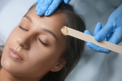 Young woman undergoing hair removal procedure on face with sugaring paste in salon, above view