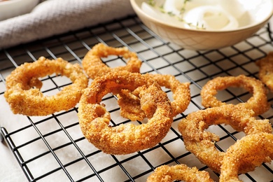 Photo of Cooling rack with homemade crunchy fried onion rings on table, closeup