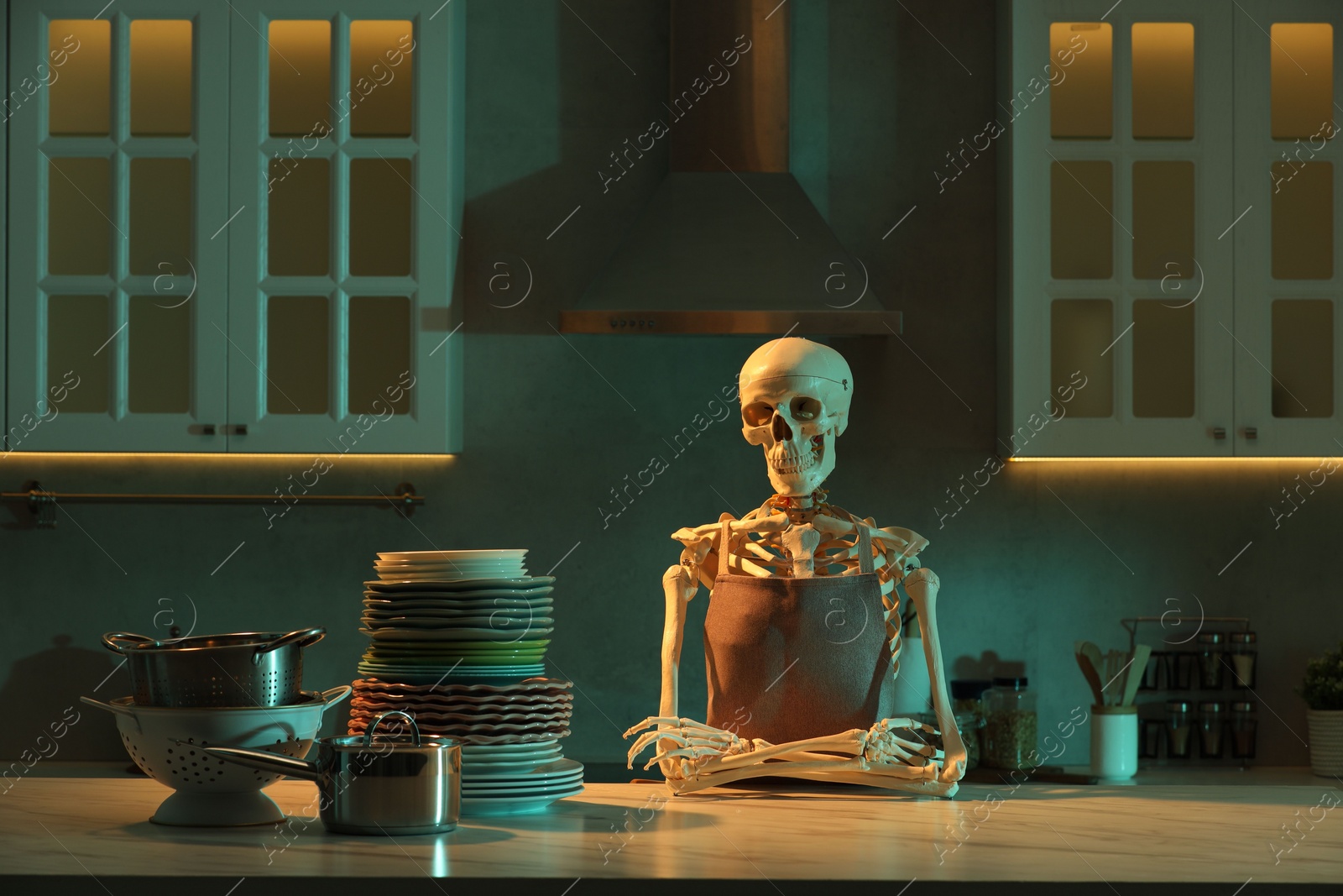 Photo of Human skeleton sitting at white marble table with clean dishware in kitchen at night