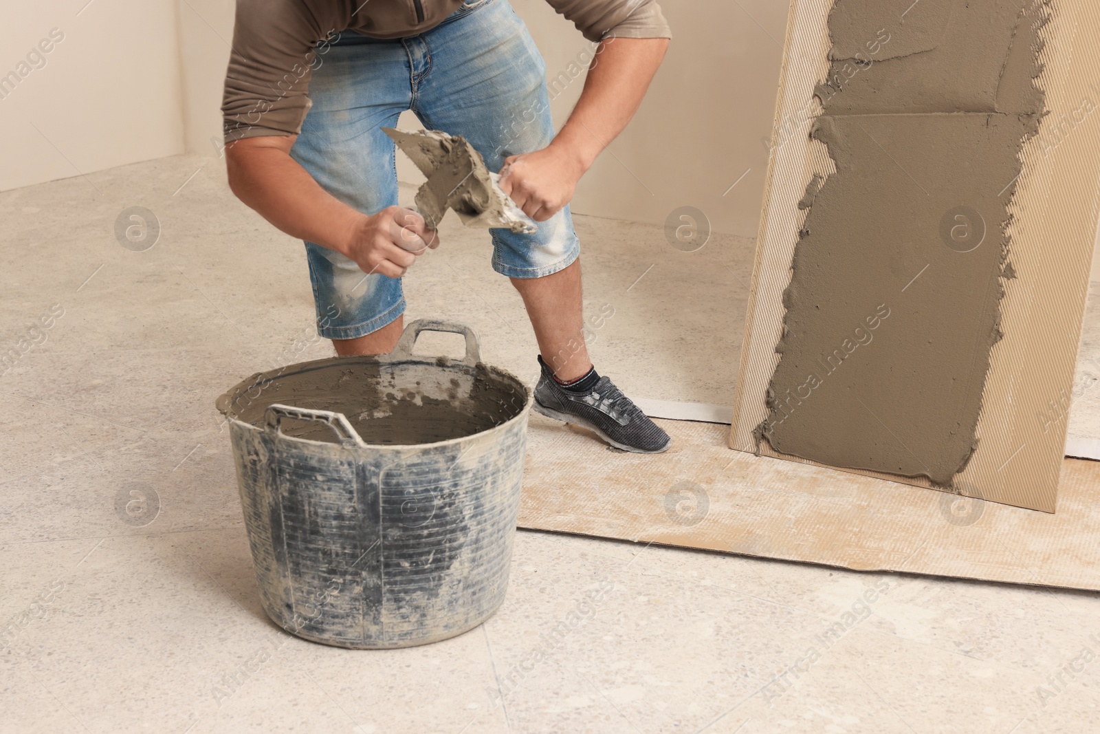 Photo of Worker applying adhesive mix on spatula near tile indoors, closeup