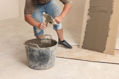 Worker applying adhesive mix on spatula near tile indoors, closeup