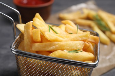 Photo of Metal basket with tasty French fries and rosemary on table, closeup