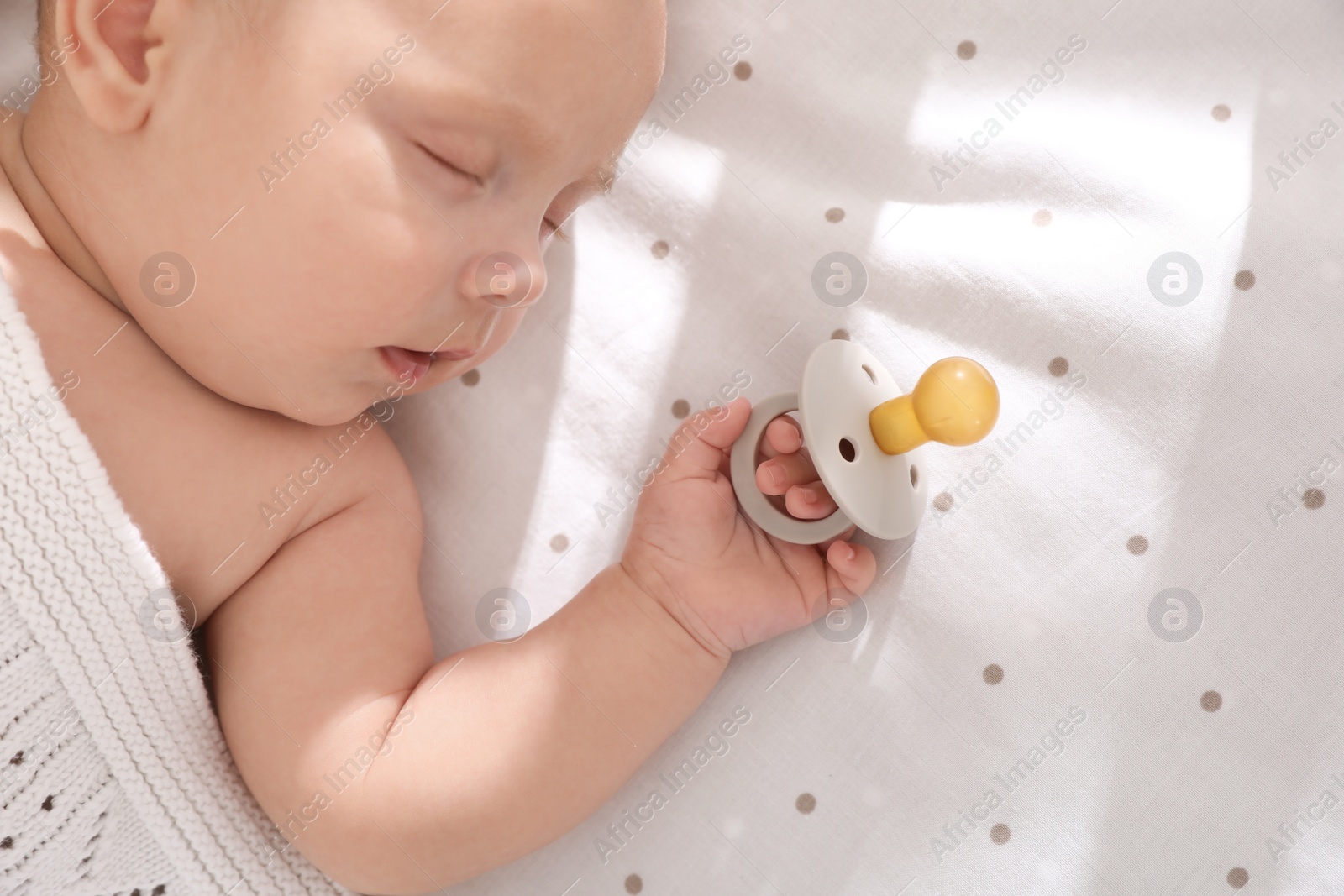 Photo of Cute little baby with pacifier sleeping in bed, top view