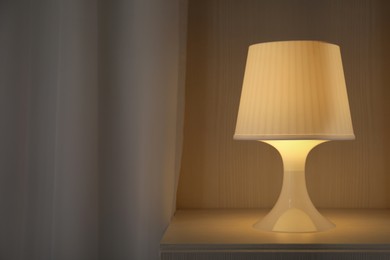 Photo of Stylish lamp on bedside table in room, space for text