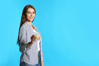 Young woman with glass of lemon water on light blue background. Space for text