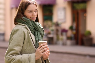 Beautiful woman in warm scarf with paper cup of coffee on city street, space for text