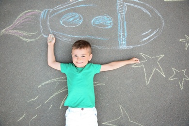 Little child lying near chalk drawing of rocket on asphalt, top view