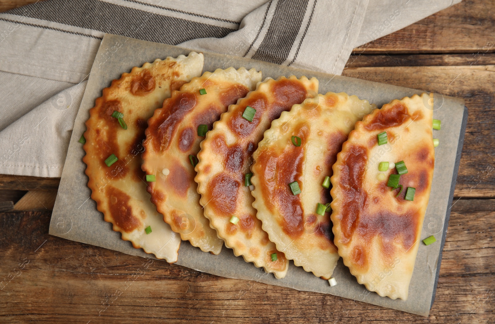 Photo of Board with delicious fried chebureki on wooden table, flat lay