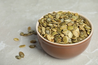 Photo of Bowl of raw pumpkin seeds on light grey marble table. Space for text