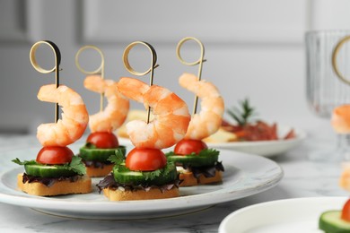 Photo of Tasty canapes with shrimps, cucumber, greens and tomatoes on white marble table, closeup