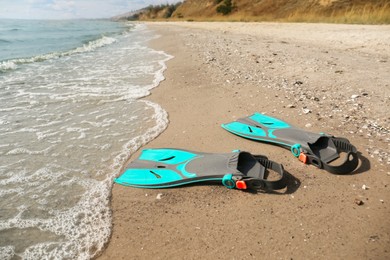 Photo of Pair of turquoise flippers on sand near sea